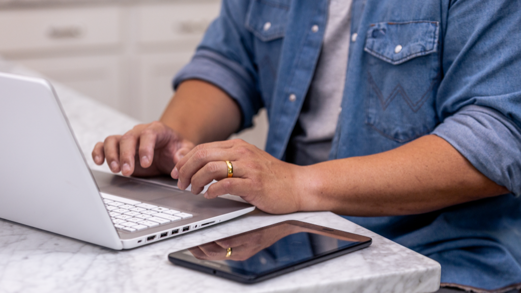 Close up of person's hands typing on laptop with tablet in foreground